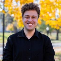 Eric Matherly headshot man with brown hair in black sweater standing in front of yellow tree in fall