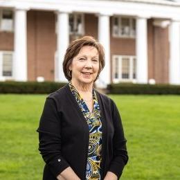 Lady with short brunette hair wearing multi colored patterned top with black cardigan standing in front of Old Centre